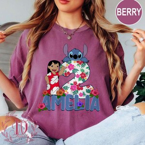 Op de afbeelding: Bessenkleurig T-shirt met een afbeelding van Lilo en Stitch met het nummer 2 versierd met bloemen. De naam "AMELIA" staat in blauwe letters onderaan. Het shirt is een comfortabele, casual stijl.