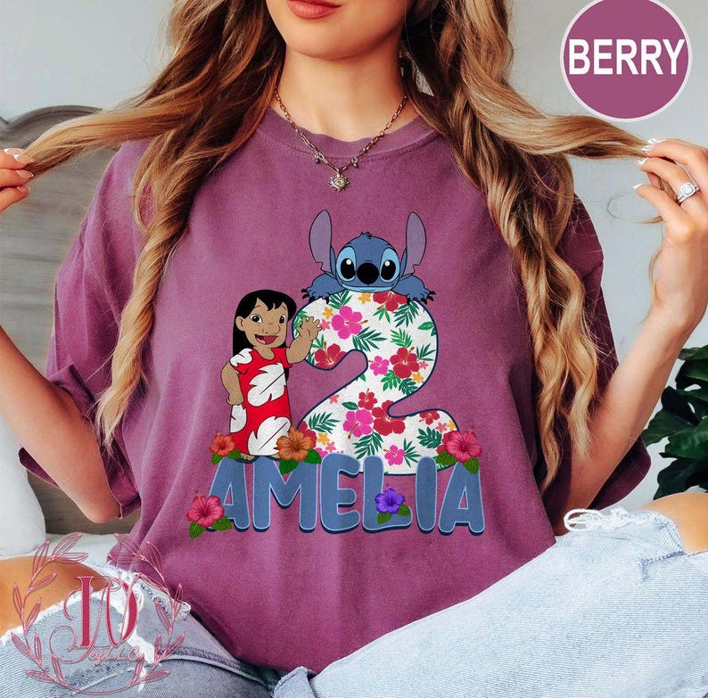 Op de afbeelding: Bessenkleurig T-shirt met een afbeelding van Lilo en Stitch met het nummer 2 versierd met bloemen. De naam "AMELIA" staat in blauwe letters onderaan. Het shirt is een comfortabele, casual stijl.