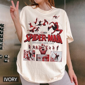 May include: Ivory-colored t-shirt featuring the Spider-Man logo and graphics from the movie. The design includes the text "SPIDER-MAN BRAND NEW DAY" in red. The shirt has a crew neck and short sleeves.