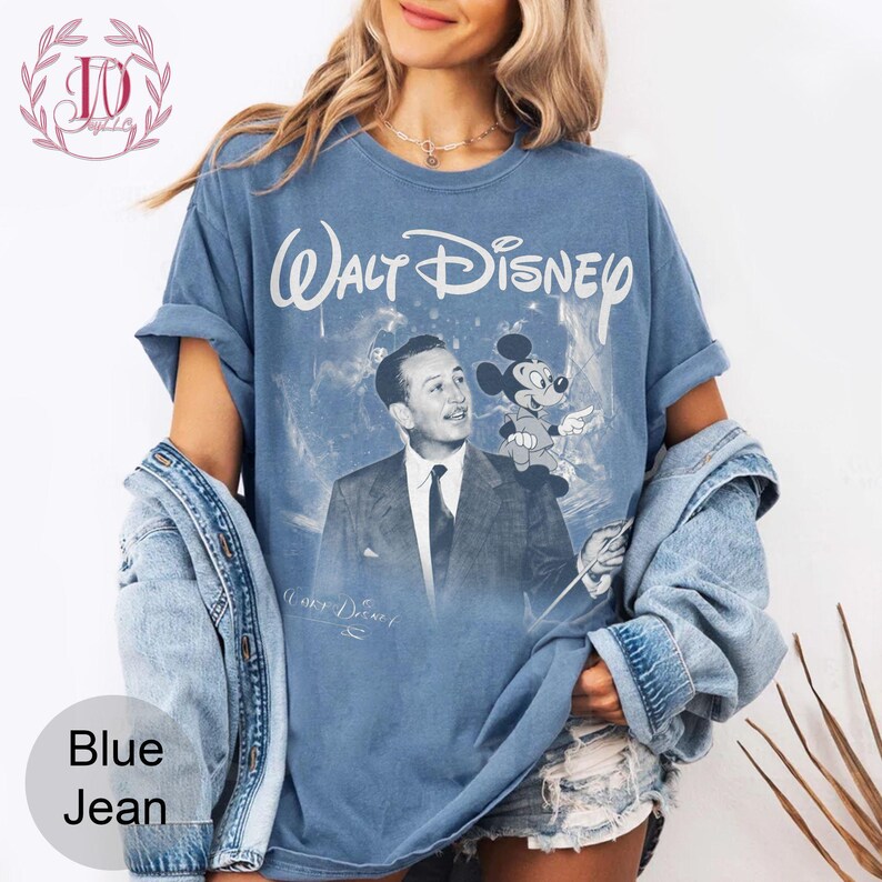 May include: Blue jean-colored t-shirt featuring a vintage graphic of Walt Disney with Mickey Mouse. The shirt has the words "Walt Disney" in white script across the top. The image includes a faded blue background and the words "Blue Jean" at the bottom.