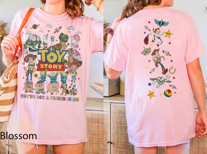May include: Pink t-shirt featuring the Toy Story logo and characters like Woody, Buzz Lightyear, and Rex. The front of the shirt displays the phrase "You've Got a Friend in Me." The back of the shirt has a design with various Toy Story characters and elements.