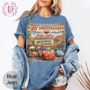 Puede incluir: Una camiseta azul con un estampado gr&aacute;fico que celebra el 20 aniversario de la pel&iacute;cula Cars. El dise&ntilde;o incluye el texto 2006 20th Anniversary 2026, un letrero de Welcome to Radiator Springs e ilustraciones de personajes como Lightning McQueen.