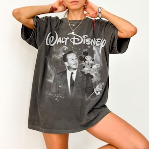 May include: Dark gray t-shirt featuring a black and white image of Walt Disney and Mickey Mouse. The shirt has the words "Walt Disney" printed in white across the top. The shirt is oversized and has short sleeves.