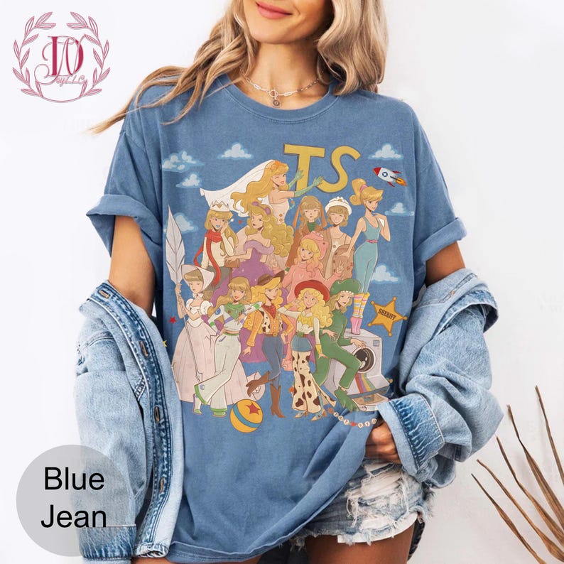 May include: A blue crew neck t-shirt featuring a graphic print of various animated characters dressed in diverse outfits, including a space suit, cowgirl attire, and formal gowns. The text TS is printed in yellow at the top with a small rocket.