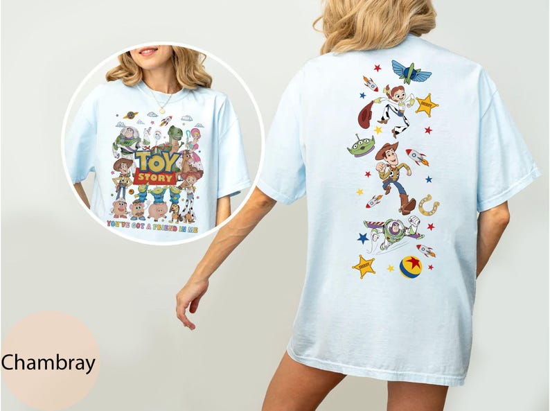 May include: Light blue t-shirt featuring a colorful graphic of Toy Story characters, including Woody, Buzz Lightyear, and others. The front of the shirt displays the Toy Story logo and the phrase "You've Got a Friend in Me."