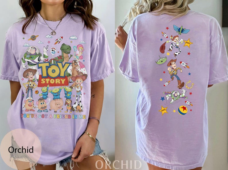 May include: A light purple t-shirt featuring characters from the animated film "Toy Story." The front of the shirt displays the movie title and various characters. The back of the shirt has additional character graphics. The text "YOU'VE GOT A FRIEND IN ME" is also on the front.