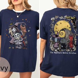 Puede incluir: Camiseta azul marino con personajes de "Pesadilla antes de Navidad". El frente muestra a Jack Skellington y otros personajes. La parte trasera muestra una luna llena y el texto "The Nightmare Before Christmas."