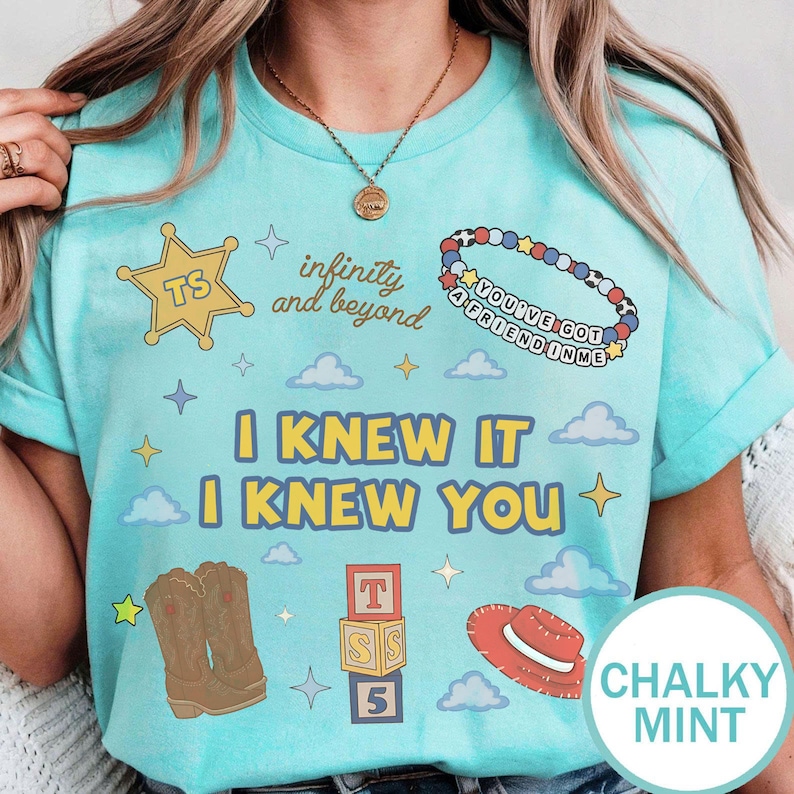 Puede incluir: Una camiseta color menta tiza con una estrella de sheriff amarilla con TS, el texto infinity and beyond, una pulsera de cuentas con el texto YOU'VE GOT A FRIEND IN ME, el texto I KNEW IT I KNEW YOU, botas vaqueras marrones y un sombrero rojo.