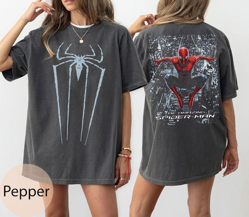May include: Dark gray t-shirt featuring a large light blue spider graphic on the front and a Spider-Man graphic on the back. The back graphic includes the text "THE AMAZING SPIDER-MAN". The shirt is a relaxed fit.