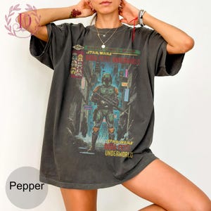 May include: Dark gray t-shirt featuring a Star Wars comic book cover with Boba Fett. The graphic includes the text "Marvel Comics Group Star Wars Boba Fett Underworld" in red, green, and yellow. The shirt has short sleeves and a relaxed fit.