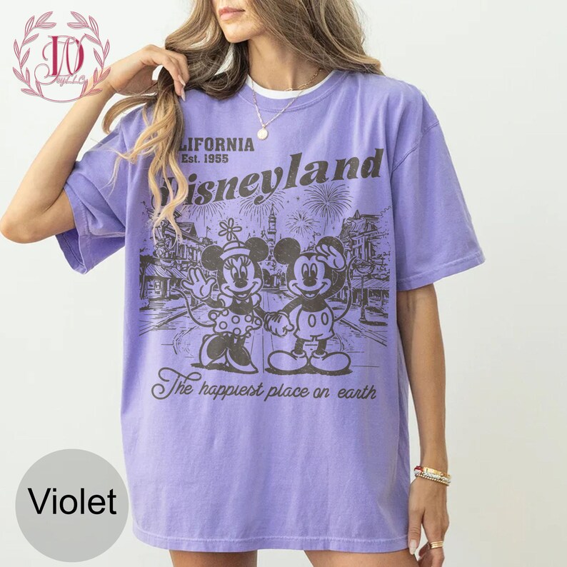 May include: Violet t-shirt with a graphic of Mickey and Minnie Mouse in front of a Disneyland scene. The shirt includes the text "California Est. 1955 Disneyland" and "The happiest place on earth."