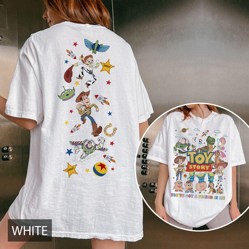 May include: White t-shirt featuring colorful graphics of characters from the animated film "Toy Story." The back of the shirt displays Woody, Buzz Lightyear, and other characters with stars and rockets. The front of the shirt has the words "Toy Story" and "You've Got a Friend in Me."