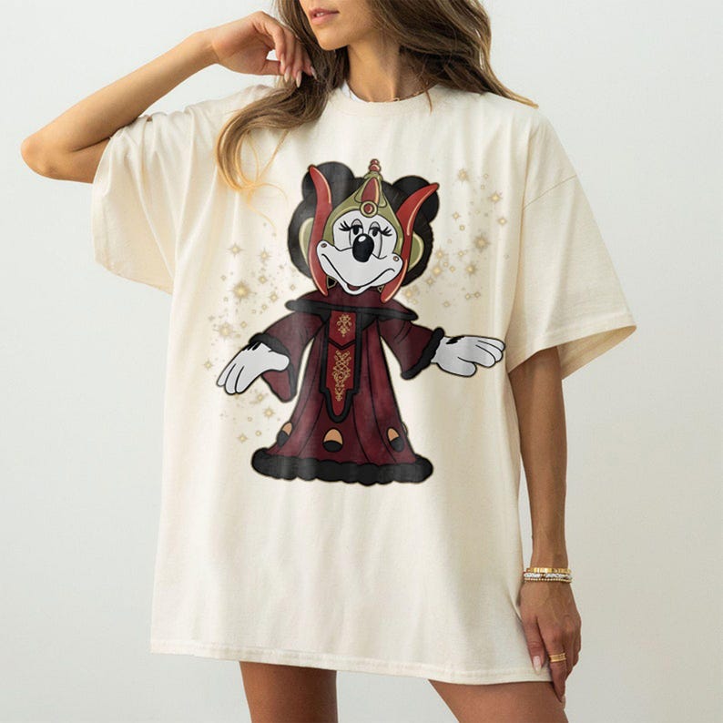 Puede incluir: Camiseta color crema con un personaje de dibujos animados con un atuendo rojo y negro con detalles dorados. El personaje tiene una cara de rat&oacute;n y lleva una corona. La camiseta tiene un corte holgado.