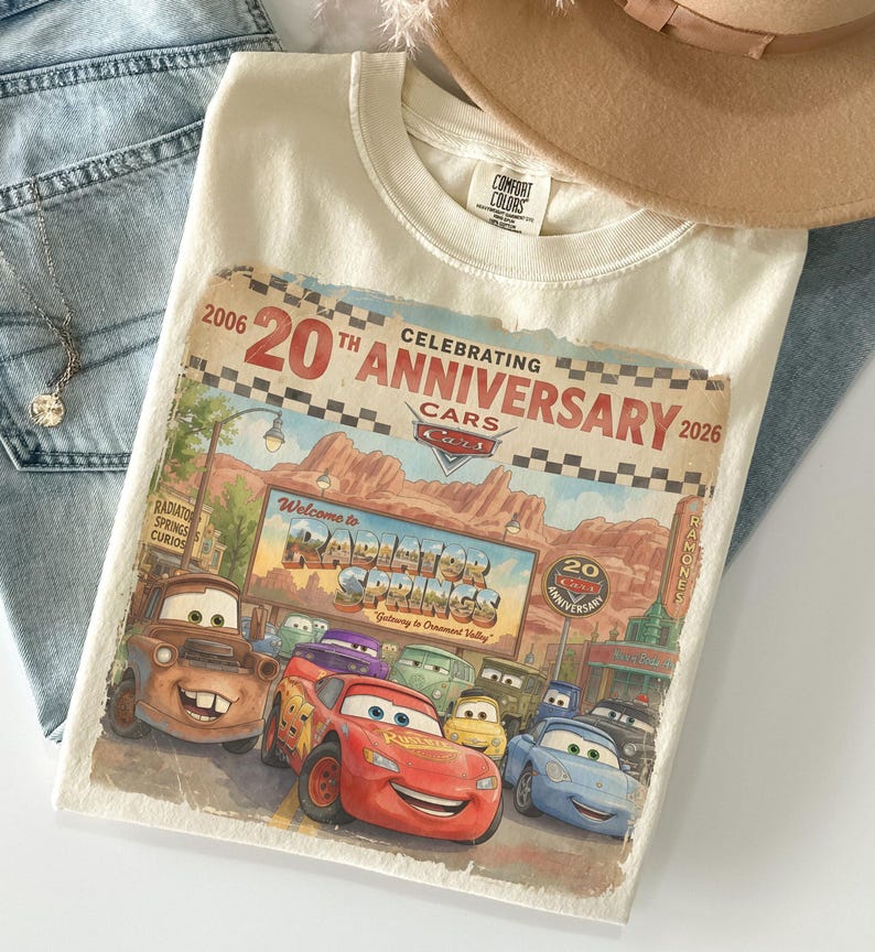 Puede incluir: Una camiseta de color crema con un estampado gr&aacute;fico que celebra el 20 aniversario de la pel&iacute;cula Cars. El dise&ntilde;o incluye personajes como Rayo McQueen y Mate frente al letrero de Radiator Springs con el texto 2006-2026.