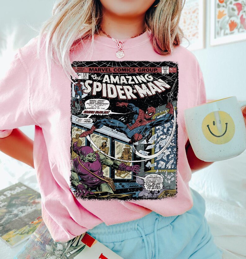 May include: Pink crew neck sweatshirt featuring a vintage comic book cover of The Amazing Spider-Man. The comic book cover shows Spider-Man in action, with the Green Goblin. The sweatshirt has a relaxed fit.