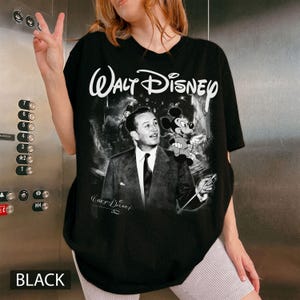 May include: Black t-shirt featuring a black and white graphic of Walt Disney and Mickey Mouse. The text "Walt Disney" is printed in white across the top. The word "BLACK" is printed in white at the bottom.