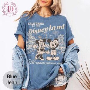 May include: Blue t-shirt with a vintage Disneyland graphic. The design features Mickey and Minnie Mouse holding hands, with the text "CALIFORNIA Est. 1955 Disneyland" and "The happiest place on earth".