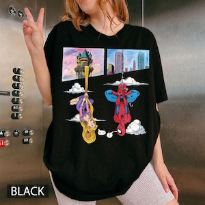 Peut inclure: T-shirt noir avec un dessin anim&eacute; de Raiponce et Spider-Man suspendus &agrave; l'envers. Raiponce est suspendue par ses longs cheveux dor&eacute;s, et Spider-Man est suspendu &agrave; une toile d'araign&eacute;e. Le mot "BLACK" est imprim&eacute; en bas.