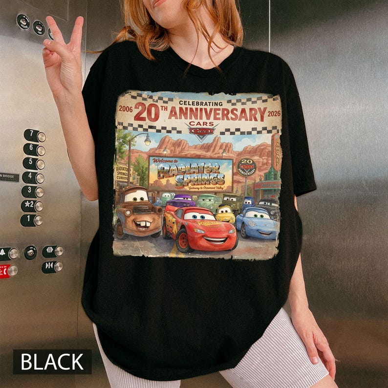 Puede incluir: Una camiseta negra con un estampado gr&aacute;fico que celebra el 20 aniversario de la pel&iacute;cula Cars. El dise&ntilde;o muestra el letrero de Radiator Springs, un borde a cuadros y varios personajes de coches, incluidos Lightning McQueen y Mater.