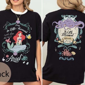 May include: Black t-shirt featuring a colorful graphic from Disney's The Little Mermaid. The front design includes Ariel, Flounder, and text. The back features Ursula and more text. The shirt has a white collar.
