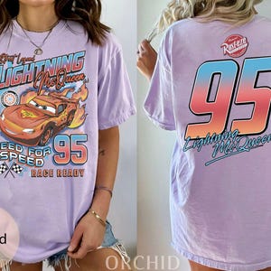 K&ouml;nnte beinhalten: Lilafarbenes T-Shirt mit Lightning McQueen aus dem Film Cars. Die Vorderseite zeigt den Text "Street Legend Lightning McQueen", ein Cartoon-Auto, die Nummer "95" und die S&auml;tze "Need for Speed" und "Race Ready". Auf der R&uuml;ckseite ist eine gro&szlig;e "95" und "Lightning McQueen" abgebildet.