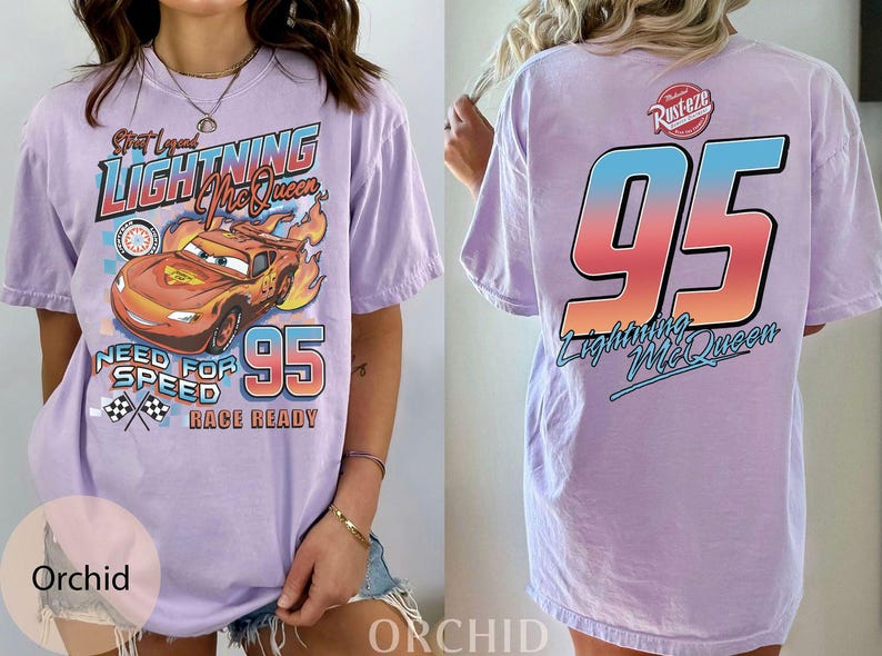 K&ouml;nnte beinhalten: Lilafarbenes T-Shirt mit Lightning McQueen aus dem Film Cars. Die Vorderseite zeigt den Text "Street Legend Lightning McQueen", ein Cartoon-Auto, die Nummer "95" und die S&auml;tze "Need for Speed" und "Race Ready". Auf der R&uuml;ckseite ist eine gro&szlig;e "95" und "Lightning McQueen" abgebildet.