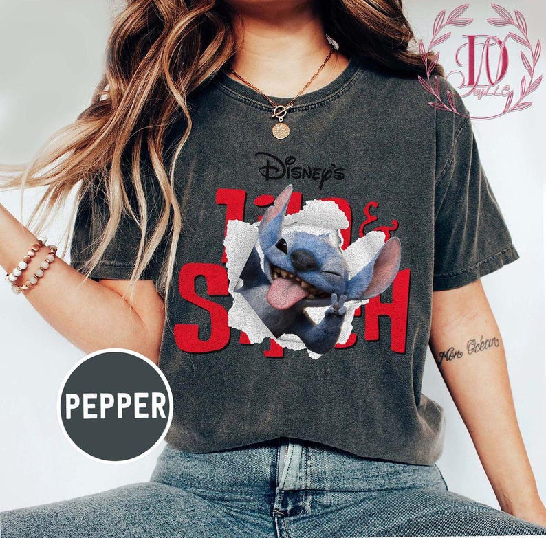 Op de afbeelding: Donkergrijs T-shirt met een afbeelding van Disney's Stitch die door een gescheurd papiereffect breekt. De tekst "Disney's Stitch" is rood. Een casual kledingstuk.