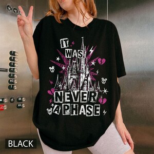 May include: Black t-shirt with a graphic design featuring a castle, lightning bolts, skulls, and the text "IT WAS NEVER A PHASE". The design incorporates purple and white elements. The word "BLACK" is at the bottom.
