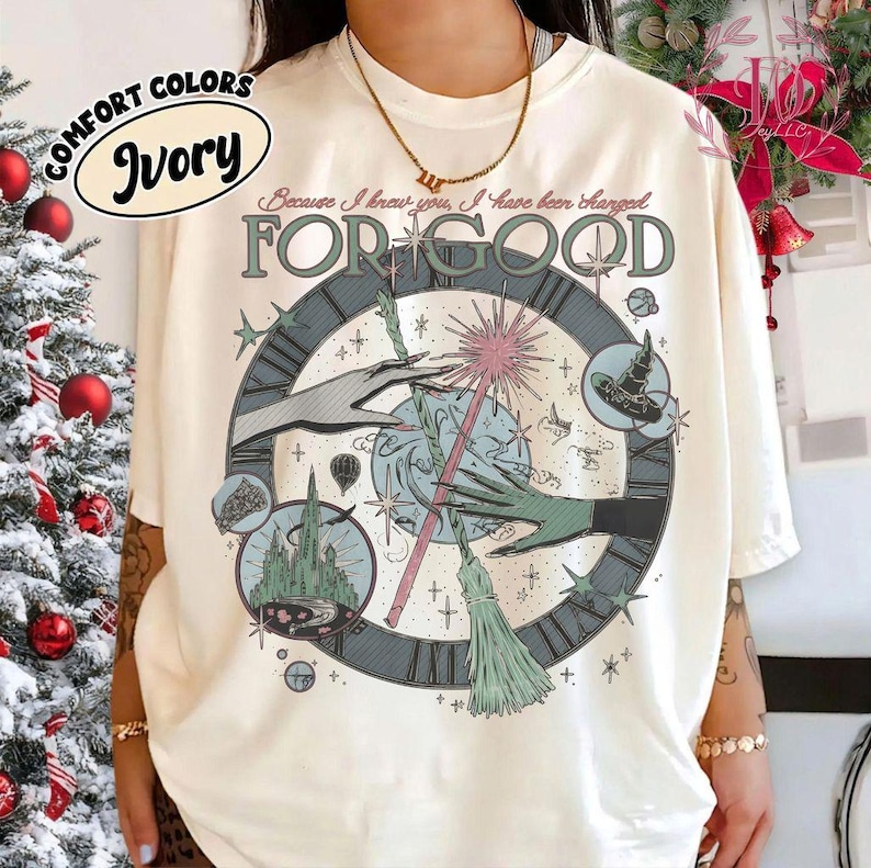 Puede incluir: Camiseta color marfil con un gr&aacute;fico que presenta un reloj, manos, una varita m&aacute;gica y una escoba. El texto "FOR GOOD" se muestra de forma destacada, con "Because I knew you, I have been charged" arriba. La camiseta tiene el texto "COMFORT COLORS" e "Ivory".