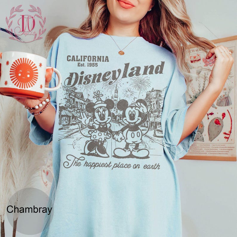 May include: Light blue t-shirt with a Disneyland graphic featuring Mickey and Minnie Mouse, fireworks, and the text "California Est. 1955." The shirt also has the phrase "The happiest place on earth."