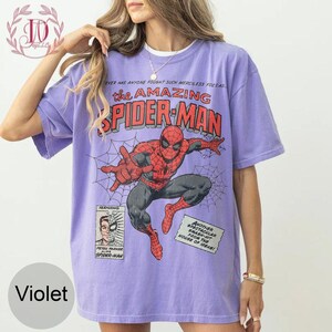 Puede incluir: Camiseta violeta con un dise&ntilde;o de c&oacute;mic de Spider-Man. El dise&ntilde;o incluye el texto "the AMAZING SPIDER-MAN" e ilustraciones del superh&eacute;roe. El texto adicional incluye "Peter Parker alias Spider-Man".
