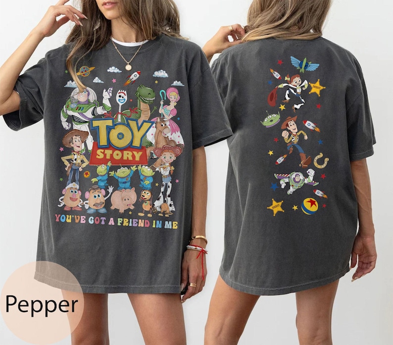 May include: Dark gray t-shirt featuring a colorful Toy Story graphic on the front and back. The front design includes characters like Buzz Lightyear and Woody, with the text "TOY STORY" and "YOU'VE GOT A FRIEND IN ME". The back has a smaller design with various characters.