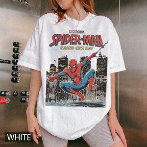 Puede incluir: Camiseta blanca con un dise&ntilde;o de Spider-Man de Marvel Studios. El dise&ntilde;o muestra a Spider-Man en una pose din&aacute;mica contra un paisaje urbano, con las palabras "SPIDER-MAN BRAND NEW DAY". La camiseta tiene cuello redondo.
