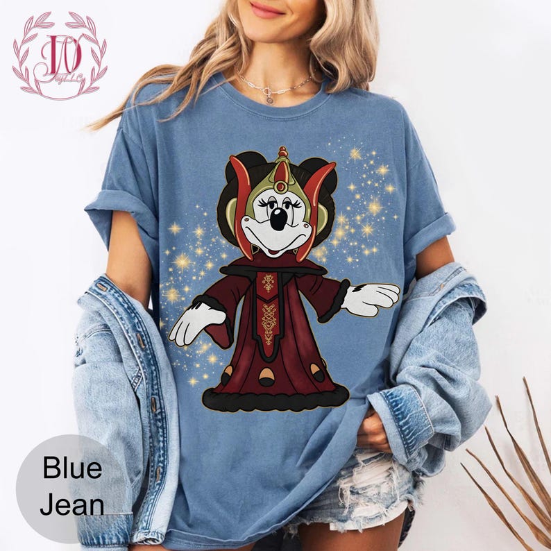 Puede incluir: Camiseta azul vaquero con un personaje de dibujos animados con un atuendo rojo y dorado. El personaje tiene un tocado negro y est&aacute; sobre un fondo de estrellas doradas. Las palabras "Blue Jean" est&aacute;n impresas en la parte inferior izquierda.
