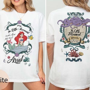 May include: White t-shirt featuring a front graphic of Ariel from Disney's The Little Mermaid, with the text "Ariel". The back graphic features Ursula, also from The Little Mermaid. The shirt has short sleeves.