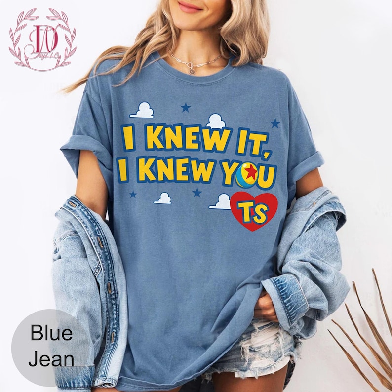 May include: A blue short-sleeve t-shirt featuring the yellow text I KNEW IT, I KNEW YOU with a colourful ball graphic replacing the letter O, a red heart with the letters TS, and white cloud and blue star graphics printed on the front.