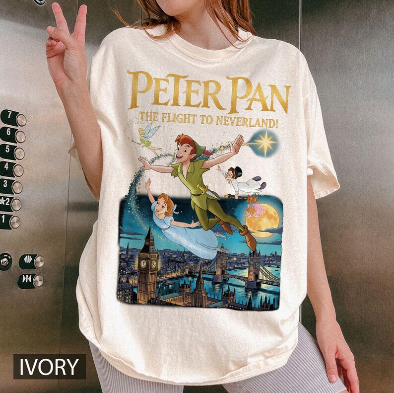 May include: Ivory t-shirt with a Peter Pan graphic, showing Peter, Wendy, Tinkerbell, and others flying over London. The text "PETER PAN THE FLIGHT TO NEVERLAND!" is printed in gold.