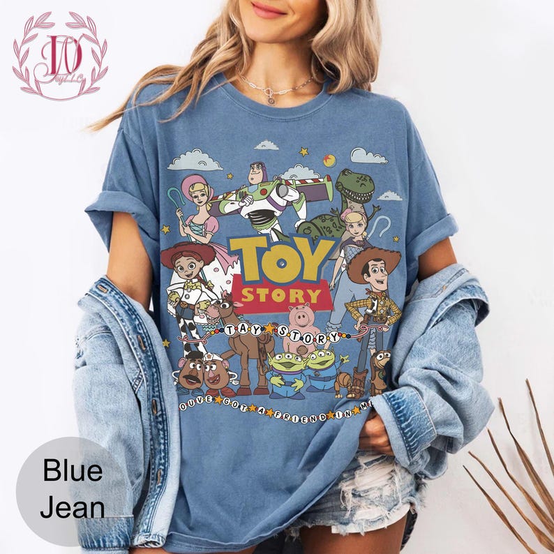 May include: A blue short-sleeve t-shirt featuring a graphic print of Toy Story characters including Woody, Buzz Lightyear, Jessie, and Rex. The design includes the text "TOY STORY" in yellow and red, along with the phrase "YOU'VE GOT A FRIEND IN ME".