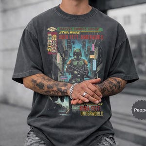 May include: Dark gray t-shirt featuring a comic book cover design. The graphic includes the text "Marvel Comics Group Star Wars Boba Fett: Underworld" and an illustration of Boba Fett. The shirt has a vintage, worn look.