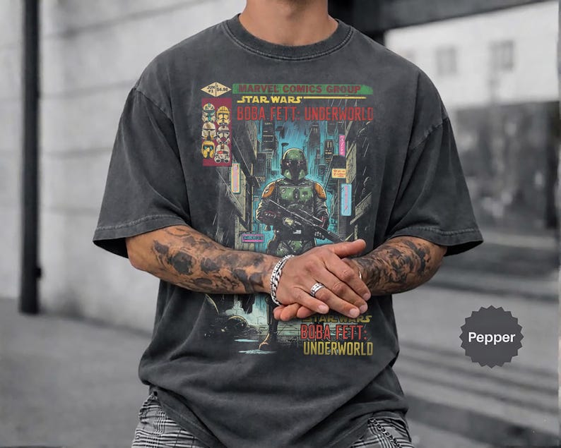 May include: Dark gray t-shirt featuring a comic book cover design. The graphic includes the text "Marvel Comics Group Star Wars Boba Fett: Underworld" and an illustration of Boba Fett. The shirt has a vintage, worn look.