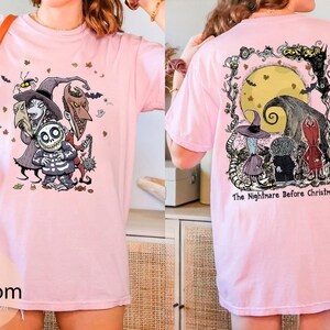 Puede incluir: Camiseta rosa claro con un gr&aacute;fico colorido de personajes de "Pesadilla antes de Navidad" en la parte delantera y trasera. El dise&ntilde;o frontal incluye a Jack Skellington y otros personajes. El dise&ntilde;o trasero presenta una luna llena y el texto "The Nightmare Before Christmas."
