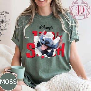 Op de afbeelding: Groen t-shirt met de tekst "Disney's Lilo & Stitch" in het rood, met een afbeelding van Stitch die door een gescheurd papiereffect breekt. Het shirt heeft korte mouwen en een relaxte pasvorm.