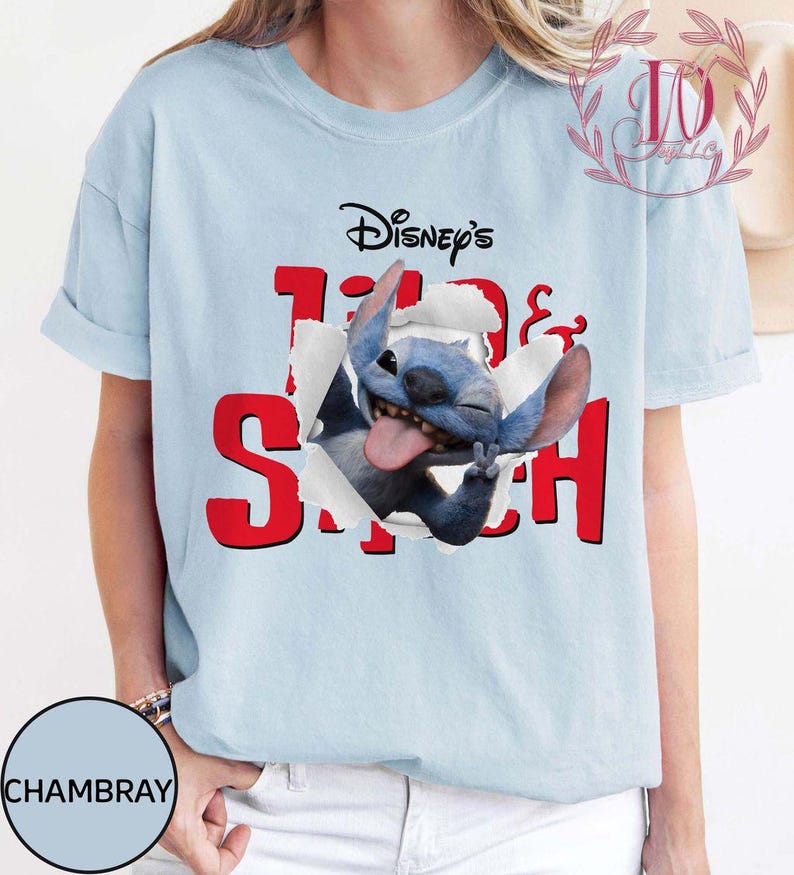 Op de afbeelding: Lichtblauw T-shirt met het Disney Stitch-personage. Het ontwerp toont Stitch die door een gescheurd papiereffect breekt met het woord "Stitch" in het rood. Het shirt is een casual kledingstuk met korte mouwen.