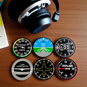May include: Six round coasters with aviation instrument designs, including airspeed, altitude, and turn coordinator gauges. The coasters are black with white and colored details. A pair of black headphones rests above them.