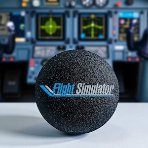 Puede incluir: Una esfera negra texturizada con la inscripción "Flight Simulator" en blanco y azul. El fondo borroso muestra una cabina de avión, sugiriendo un tema de aviación y simulación.
