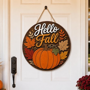 Puede incluir: Un letrero circular de madera para puerta con el texto Hello Fall en letra cursiva blanca y naranja. El diseño incluye una gran calabaza naranja en el centro rodeada de hojas de madera superpuestas en tonos rojo, naranja, amarillo y verde.