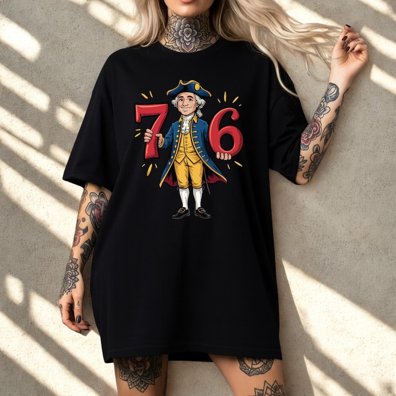 May include: Black t-shirt with a cartoon illustration of a man in colonial clothing holding the numbers "76". The man wears a blue coat, yellow vest, and white trousers. The numbers are red with yellow accents. The design celebrates a historical theme.