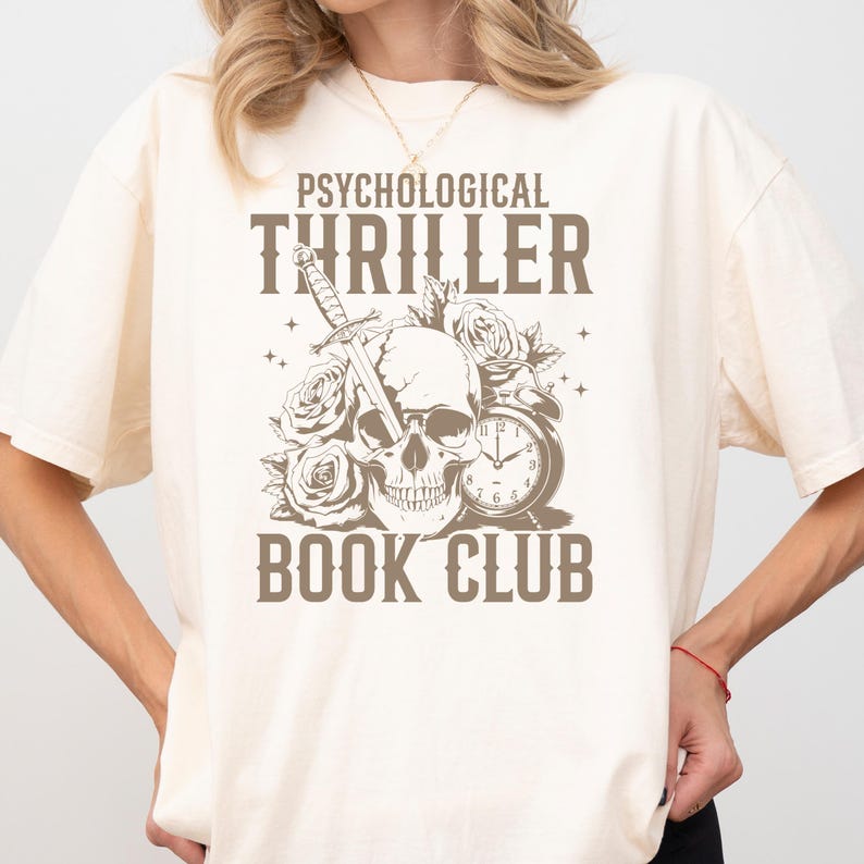 May include: Cream-colored t-shirt with a graphic design featuring a skull pierced by a sword, surrounded by roses and an antique clock. The text reads "PSYCHOLOGICAL THRILLER BOOK CLUB" in a dark brown color.