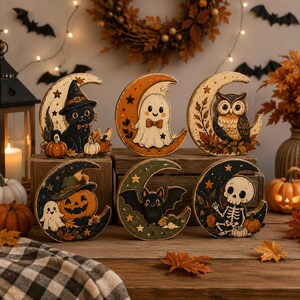 Peut inclure: Un ensemble de six décorations en bois en forme de croissant de lune avec des illustrations d'Halloween. Les motifs incluent un chat noir avec un chapeau de sorcière, un fantôme, un hibou, une citrouille, une chauve-souris et un squelette.