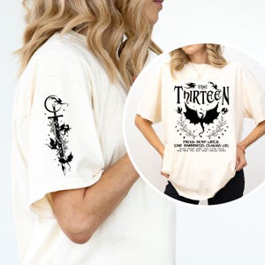 May include: A white t-shirt with a black graphic print of a dragon and the text "The Thirteen" and "From now until the darkness claims us".